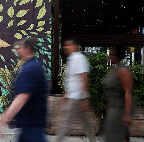 People walking past a cafe planted with greenery