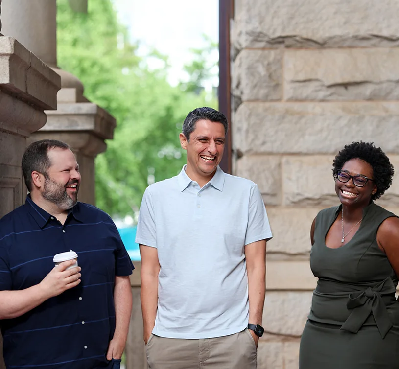 Three colleagues laughing together outside a stone building