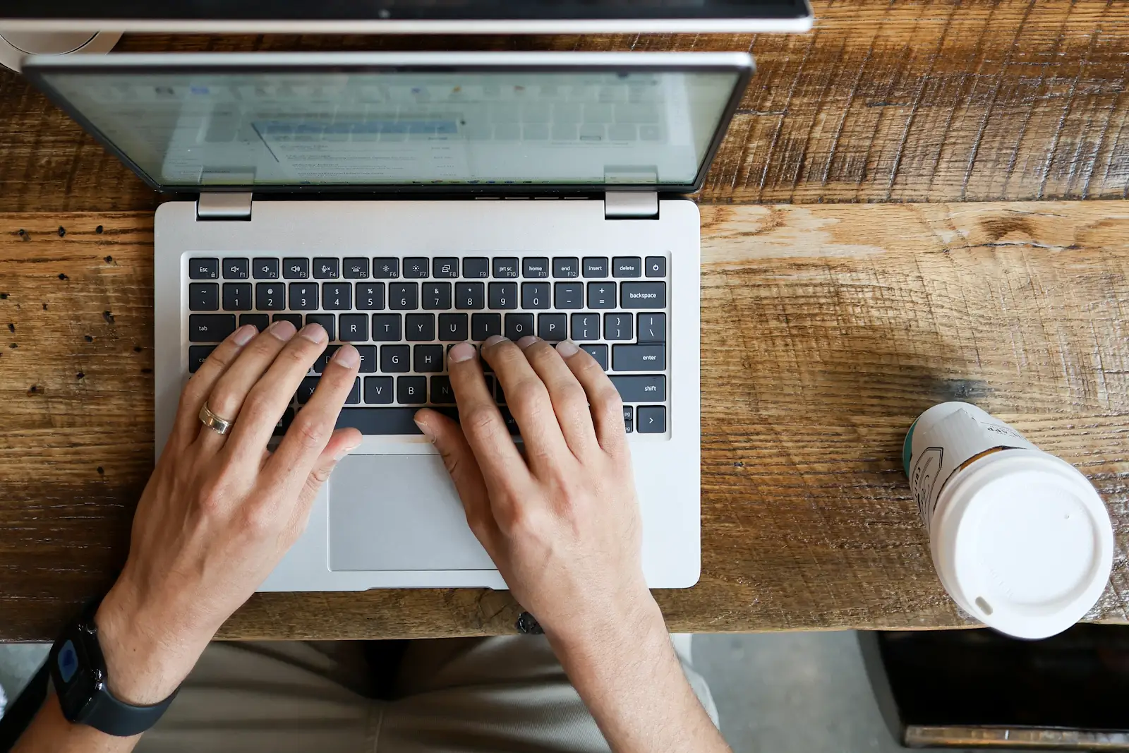 Hands typing on a laptop on a wooden table, seen from above