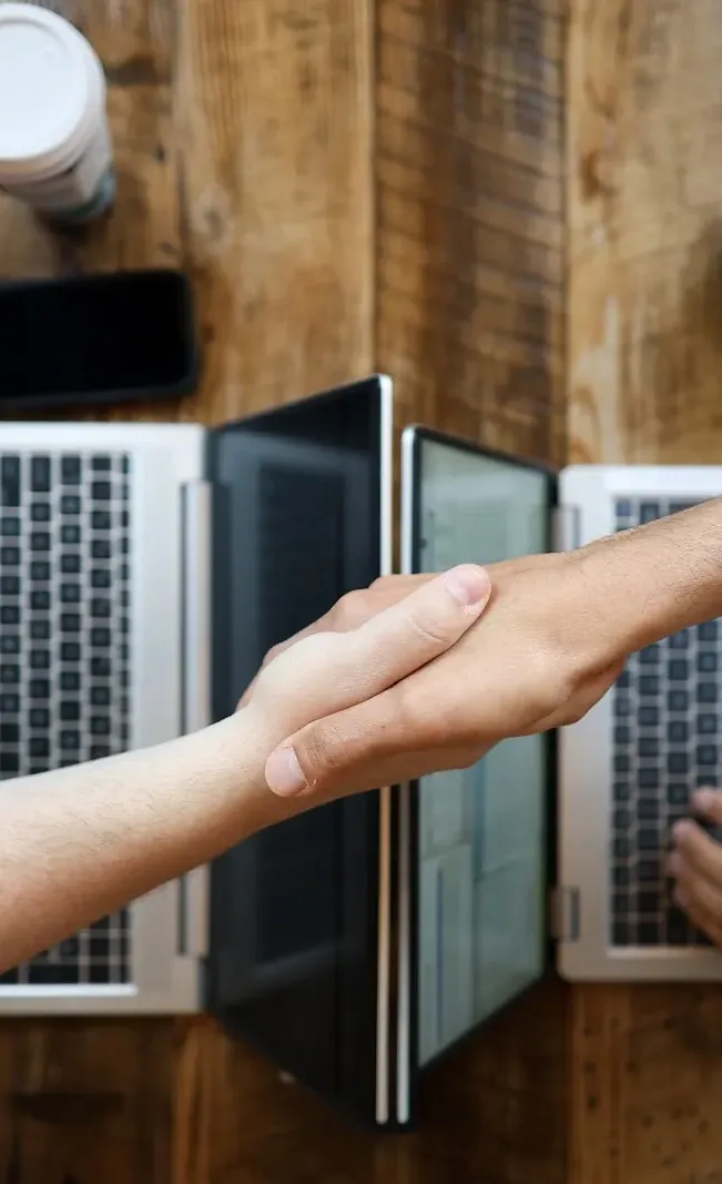 Two people shaking hands between two laptops, seen from above