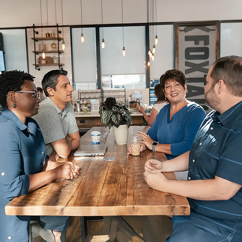Four people talking around a long table in a coffee shop