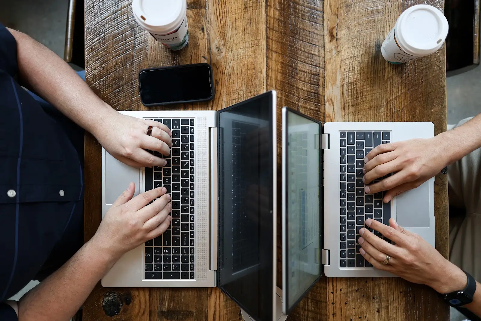 Two people working on laptops at a wooden table, seen from above